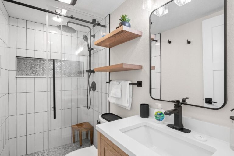 Remodeled master bathroom with walk-in glass shower white subway tile and wood shelves in Florida beach rental