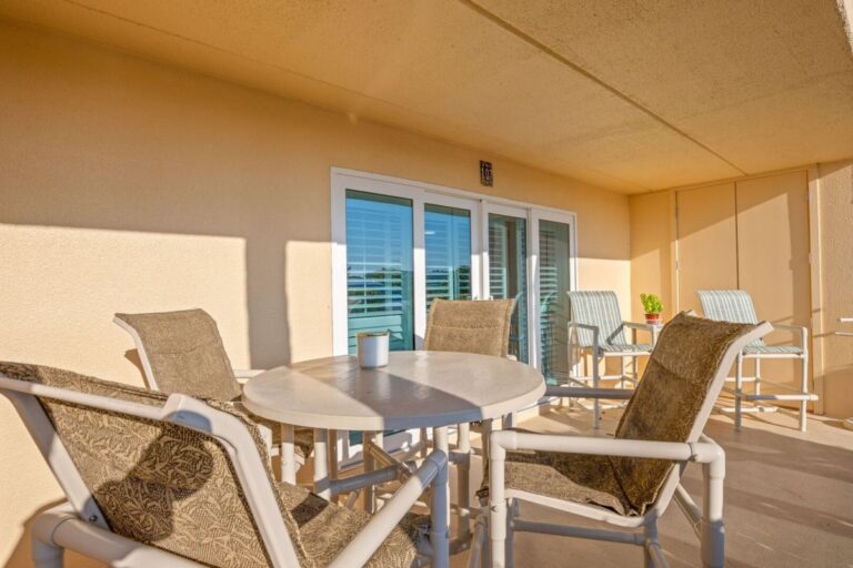 Covered patio balcony with lounge chairs and dining set overlooking palm trees at Fifty Gulfside condos
