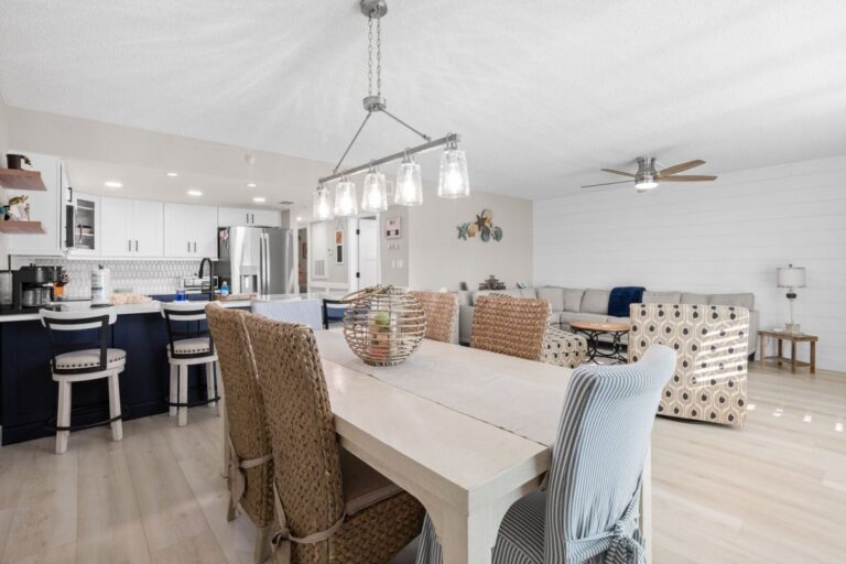 Dining table with wicker chairs overlooking remodeled kitchen with navy blue cabinets at Fifty Gulfside Unit 107