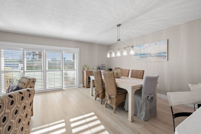 Remodeled dining area with wicker chairs and coastal beach artwork in Unit 107 Indian Rocks Beach condo