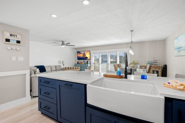 Navy blue kitchen island with white farmhouse sink and living room with WiFi sign in Fifty Gulfside condo